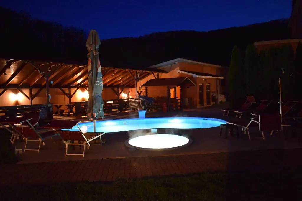 Piscina încălzită iluminată la apus, cu șezlonguri pe terasă